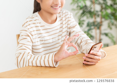 A middle school girl making a circle sign with her fingers while operating a smartphone at home A middle school girl making a circle sign with her fingers while operating a smartphone at home 129376838