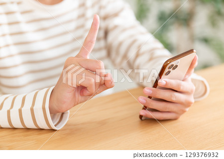A middle school girl raising her index finger while operating a smartphone at home 129376932