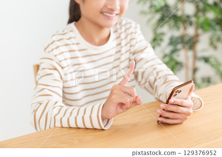 A middle school girl raising her index finger while operating a smartphone at home 129376952