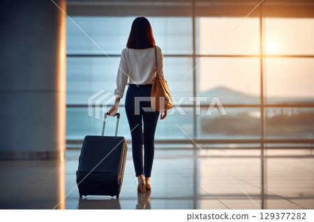 Woman Traveling Alone with Suitcase in Airport Terminal During Sunset with Beautiful Light 129377282