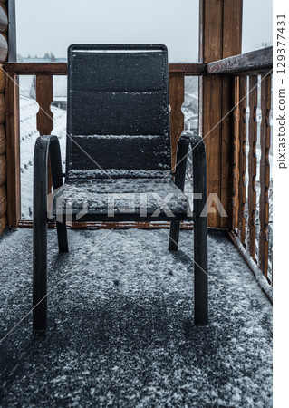 snow-covered armchair on balcony in serene winter setting during snowfall. closeup. snow-covered armchair on balcony in serene winter setting during snowfall. closeup. 129377431