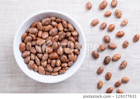 Pinto beans, in a white bowl, on linen fabric. Dried variety of common beans, Phaseolus vulgaris. Type of bean that are tan with reddish-brown specks. Most popular bean in Mexico and Southwestern USA. Pinto beans, in a white bowl, on linen fabric. Dried variety of common beans, Phaseolus vulgaris. Type of bean that are tan with reddish-brown specks. Most popular bean in Mexico and Southwestern USA. 129377631