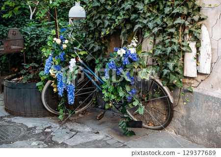 Old bicycle repurposed as a garden decoration with cascading blue and white flowers, leaning against a vine-covered wall. Upcycled decor, creative reuse, sustainable design, circular creativity Old bicycle repurposed as a garden decoration with cascading blue and white flowers, leaning against a vine-covered wall. Upcycled decor, creative reuse, sustainable design, circular creativity 129377689