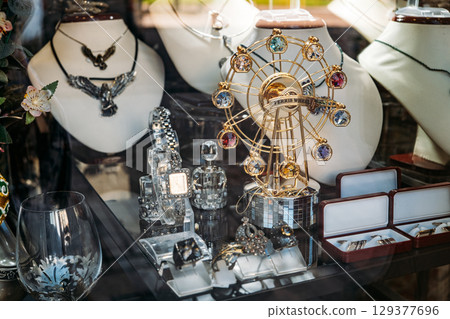 Close-up of a jewelry shop window featuring ornate rings, luxury watches, and a Ferris wheel-themed gem display. Luxury accessories, visual merchandising, gift economy, retail storytelling Close-up of a jewelry shop window featuring ornate rings, luxury watches, and a Ferris wheel-themed gem display. Luxury accessories, visual merchandising, gift economy, retail storytelling 129377696