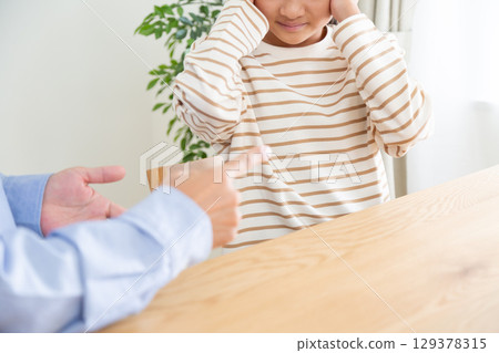 A middle school girl covers her ears after being scolded by her father 129378315