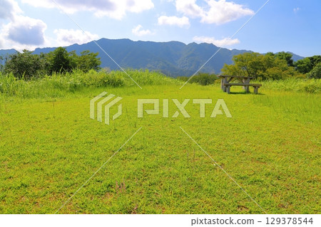 Grassland, trees, blue sky, clouds, mountains, table, bench 129378544