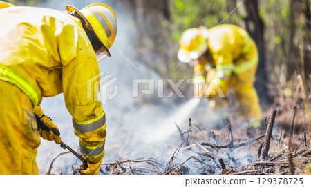 Firefighters combat forest wildfire in protective gear, creating dense smoke 129378725