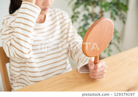 A middle school girl checking her skin in a hand mirror 129379197