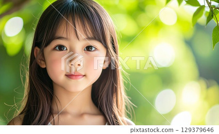 Portrait of a girl against a green background with sunlight filtering through the trees 129379646