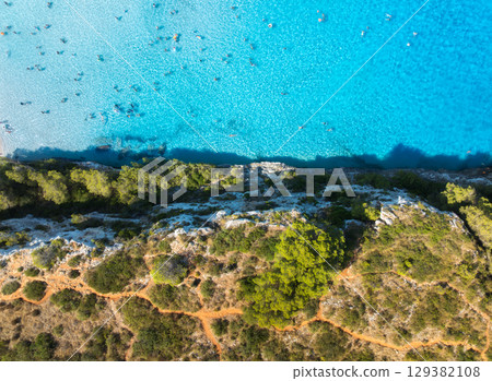 Aerial drone view of turquoise sea, swimmers, rocky coastline 129382108