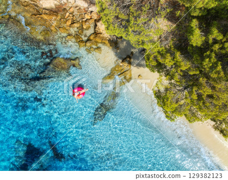Aerial view of woman on pink inflatable ring in blue sea 129382123