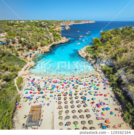 Aerial view of colorful umbrellas on sandy beach, swimming people 129382164