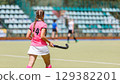 Field hockey player in pink uniform prepares for action during a match 129382201