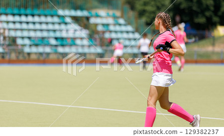 Young athlete plays field hockey in bright pink uniform. Copy space image 129382237