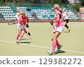 Competitive field hockey players engaged in a match on a sunny day 129382272