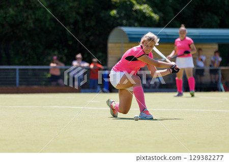 Field hockey player hitting the ball under the bright sun during a game Field hockey player hitting the ball under the bright sun during a game 129382277