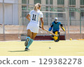 Female forward attacking the goalkeeper in a field hockey game 129382278
