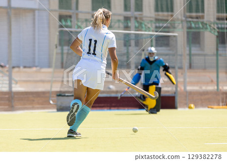Female forward attacking the goalkeeper in a field hockey game 129382278