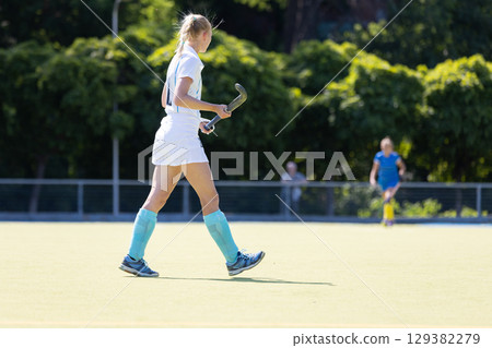 Field hockey player walks on a sunny day during a game at a sports facility 129382279