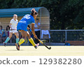 Competitive field hockey match featuring players in action at a sunny outdoor venue 129382280