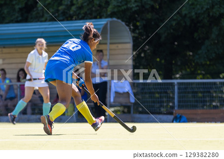 Competitive field hockey match featuring players in action at a sunny outdoor venue Competitive field hockey match featuring players in action at a sunny outdoor venue 129382280