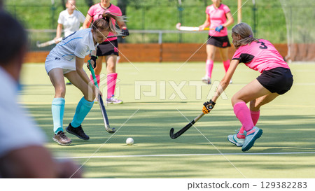 Competitive field hockey match featuring players in action on sunny day Competitive field hockey match featuring players in action on sunny day 129382283