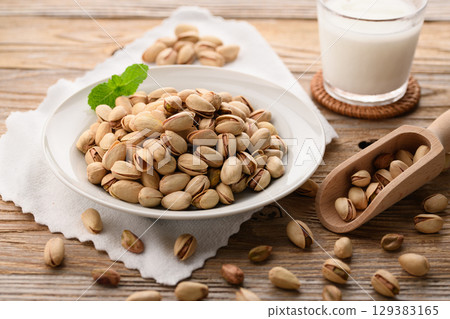 香氣撲鼻的開心果和牛奶。一幅自然時尚的食物圖片，以木紋背景和白色布料為背景。 129383165