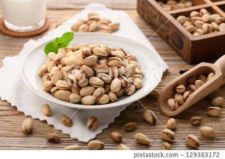 香氣撲鼻的開心果和牛奶。一幅自然時尚的食物圖片,以木紋背景和白色布料為背景。 香氣撲鼻的開心果和牛奶。一幅自然時尚的食物圖片,以木紋背景和白色布料為背景。 129383172