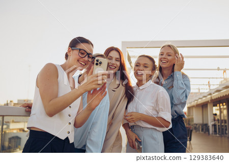 A joyful group of friends happily taking a cheerful selfie outdoors, smiling and laughing 129383640