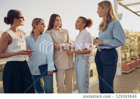 Women Networking Outdoors While Dressed in Elegant Attire and Accessories Enjoying the Event 129383648