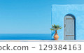 Beautiful blue wall with wooden door and potted palm against a clear sky and ocean view 129384163