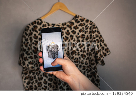 Girl takes pictures of her old wardrobe items to sell secondhand. Minimalist background. Focus on eco friendly consumer habits. 129384540