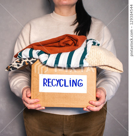 Woman prepared cardboard box full of used outfits for recycling. Responsible disposal and secondhand fashion concept. 129384544