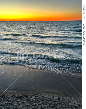 Sunset gradient from blue to orange above blue ocean water with small waves. Sunset gradient from blue to orange above blue ocean water with small waves. 129384555