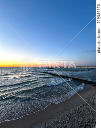 Golden sunset over calm sea with wooden pier stretching into water. Meditation content, moody aesthetics. 129384556