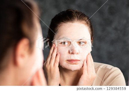 Female applying moisturizing face mask in bathroom. Beauty routine. International Self Care Day. 129384559