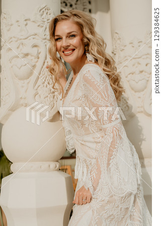 Beautiful slim blonde poses in boho wedding dresses and an embroidered corset on a summer terrace 129384625