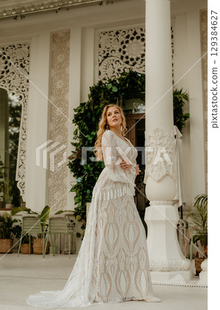 Beautiful slim blonde poses in boho wedding dresses and an embroidered corset on a summer terrace Beautiful slim blonde poses in boho wedding dresses and an embroidered corset on a summer terrace 129384627