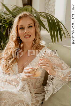 Beautiful slim blonde poses in boho wedding dresses and an embroidered corset on a summer terrace Beautiful slim blonde poses in boho wedding dresses and an embroidered corset on a summer terrace 129384635