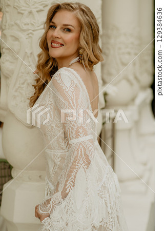 Beautiful slim blonde poses in boho wedding dresses and an embroidered corset on a summer terrace Beautiful slim blonde poses in boho wedding dresses and an embroidered corset on a summer terrace 129384636
