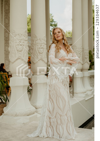 Beautiful slim blonde poses in boho wedding dresses and an embroidered corset on a summer terrace 129384637