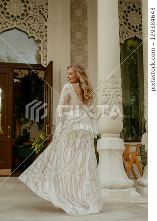 Beautiful slim blonde poses in boho wedding dresses and an embroidered corset on a summer terrace 129384643