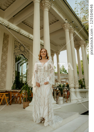 Beautiful slim blonde poses in boho wedding dresses and an embroidered corset on a summer terrace Beautiful slim blonde poses in boho wedding dresses and an embroidered corset on a summer terrace 129384646