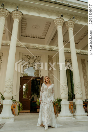Beautiful slim blonde poses in boho wedding dresses and an embroidered corset on a summer terrace 129384647
