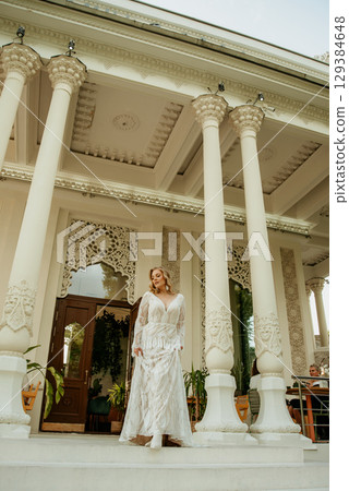 Beautiful slim blonde poses in boho wedding dresses and an embroidered corset on a summer terrace Beautiful slim blonde poses in boho wedding dresses and an embroidered corset on a summer terrace 129384648