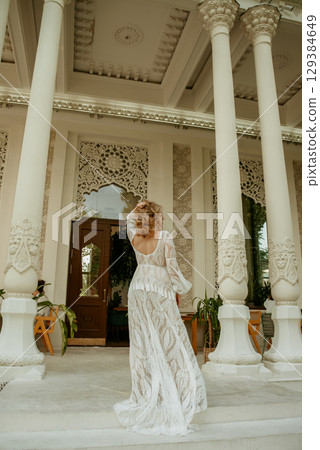 Beautiful slim blonde poses in boho wedding dresses and an embroidered corset on a summer terrace 129384649