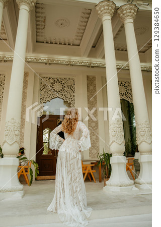 Beautiful slim blonde poses in boho wedding dresses and an embroidered corset on a summer terrace 129384650