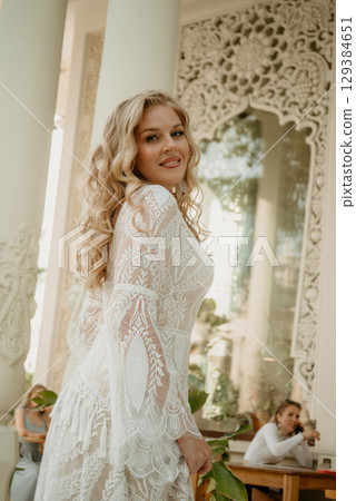 Beautiful slim blonde poses in boho wedding dresses and an embroidered corset on a summer terrace Beautiful slim blonde poses in boho wedding dresses and an embroidered corset on a summer terrace 129384651