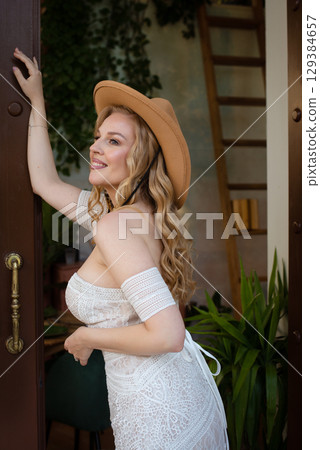 Beautiful slim blonde poses in boho wedding dresses and an embroidered corset on a summer terrace Beautiful slim blonde poses in boho wedding dresses and an embroidered corset on a summer terrace 129384657