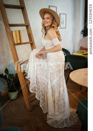 Beautiful slim blonde poses in boho wedding dresses and an embroidered corset on a summer terrace Beautiful slim blonde poses in boho wedding dresses and an embroidered corset on a summer terrace 129384659